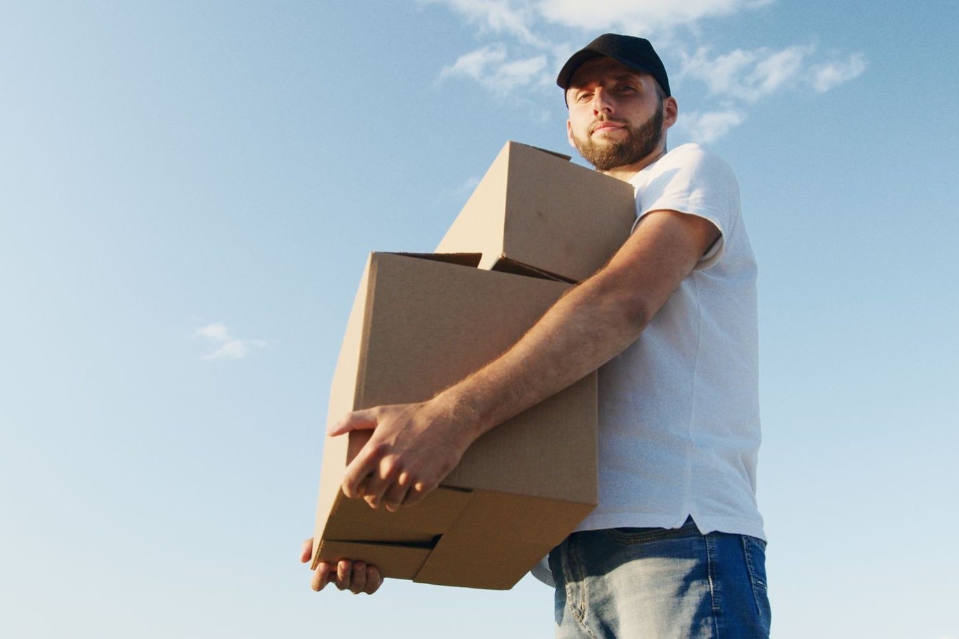 A mover carrying two stacked cartons on his shoulder against an open sky.