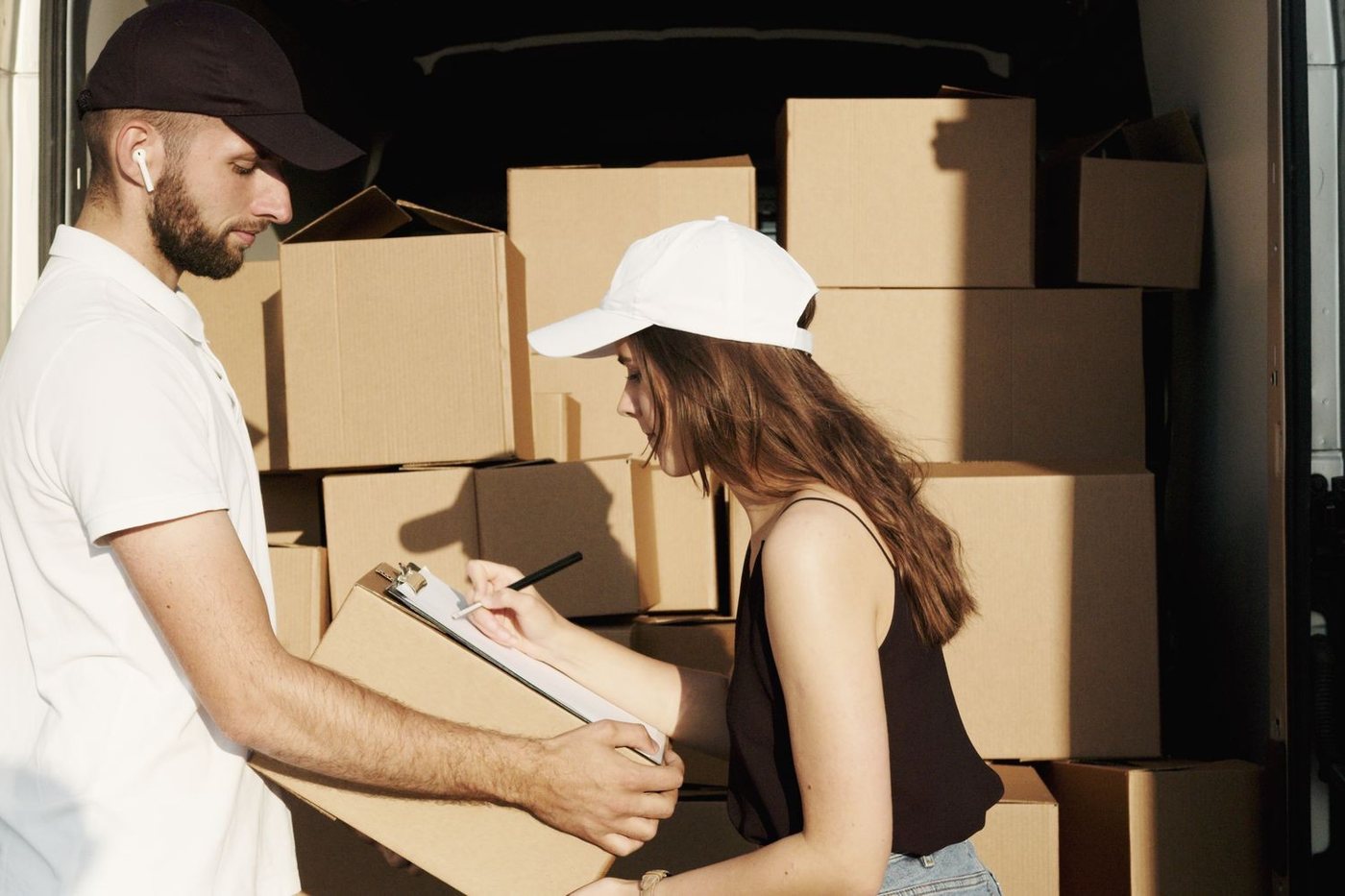 A mover and a customer checking the inventory on a clipboard beside a van packed with cartons.