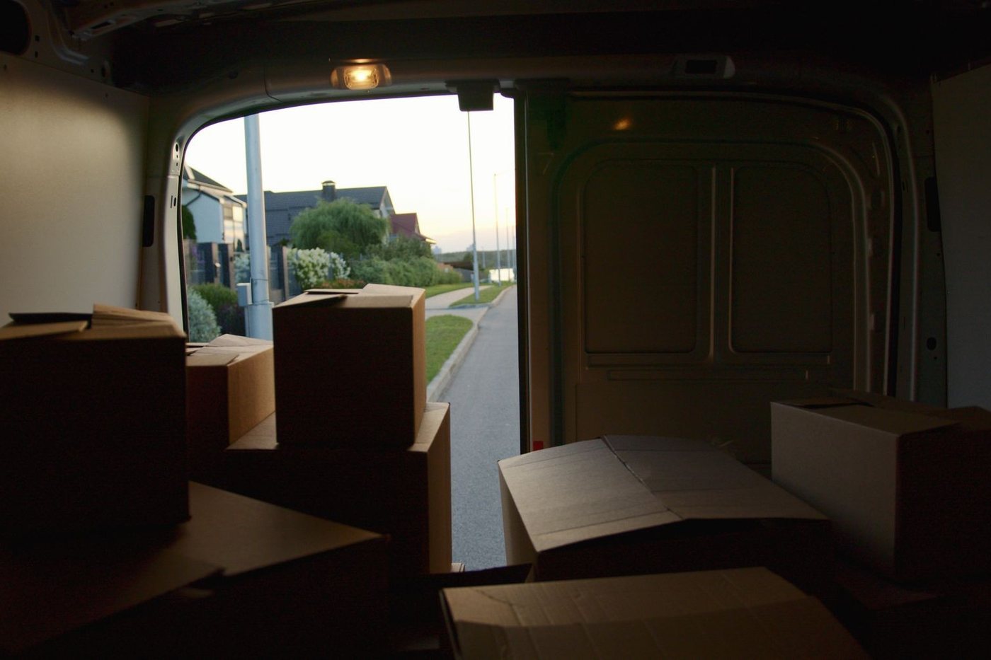 The inside of a loaded van looking out through the open rear doors onto a street at dusk.